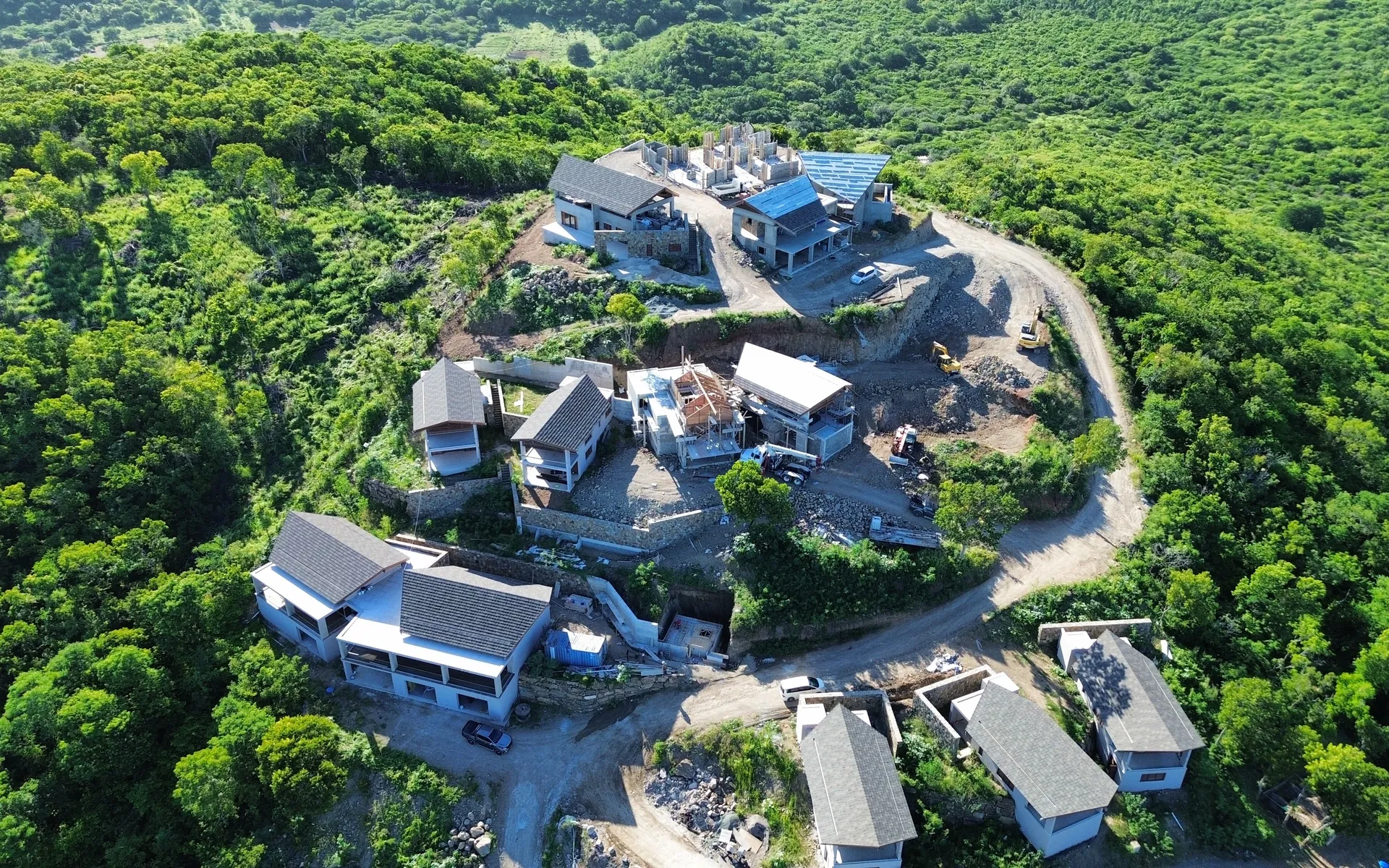 Aerial view of homes at different stages of construction along a hillside road in Antigua
