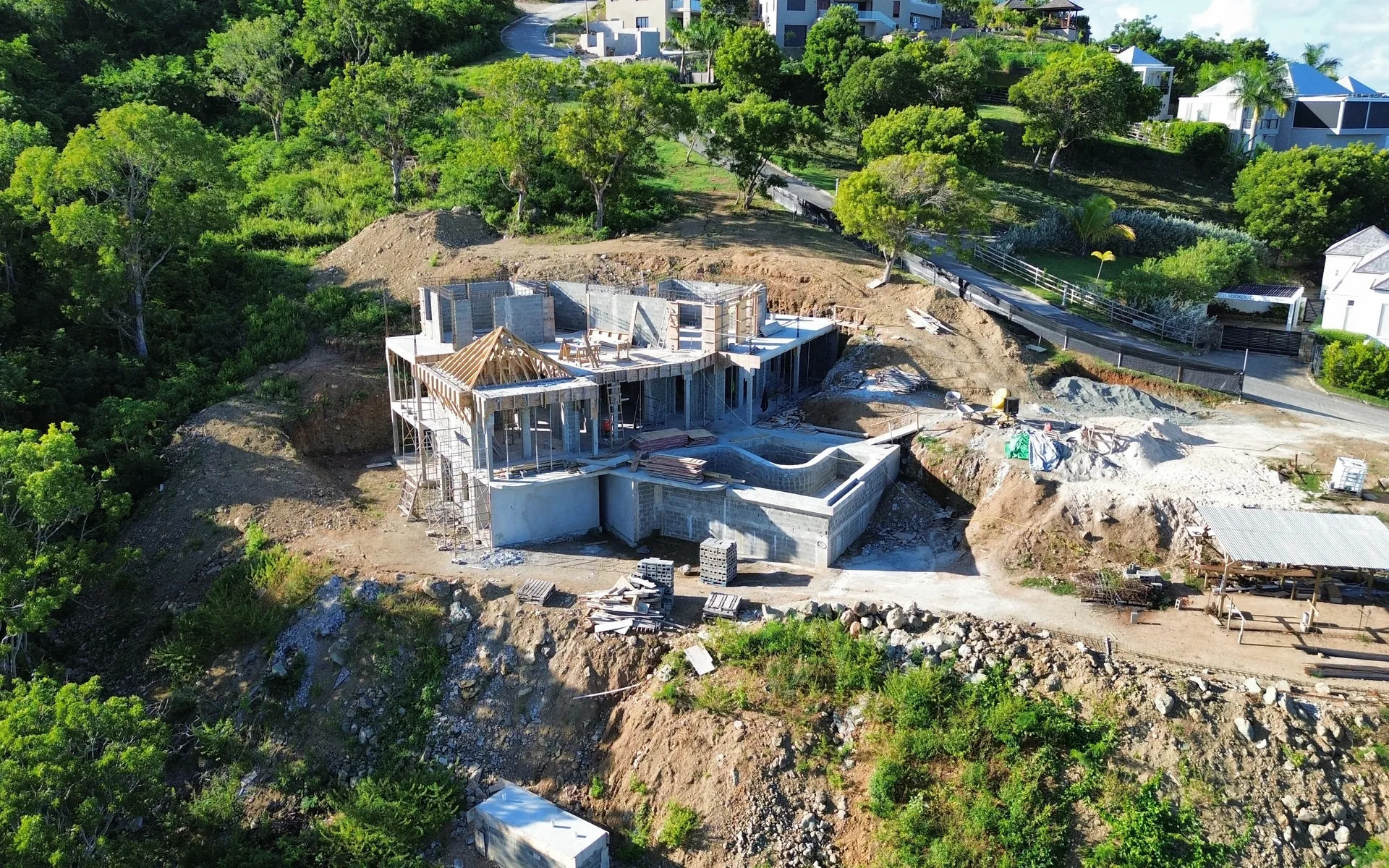 Aerial view of a villa under construction on a cut hillside in Antigua, its concrete frame and pool shell rising above the excavated slope