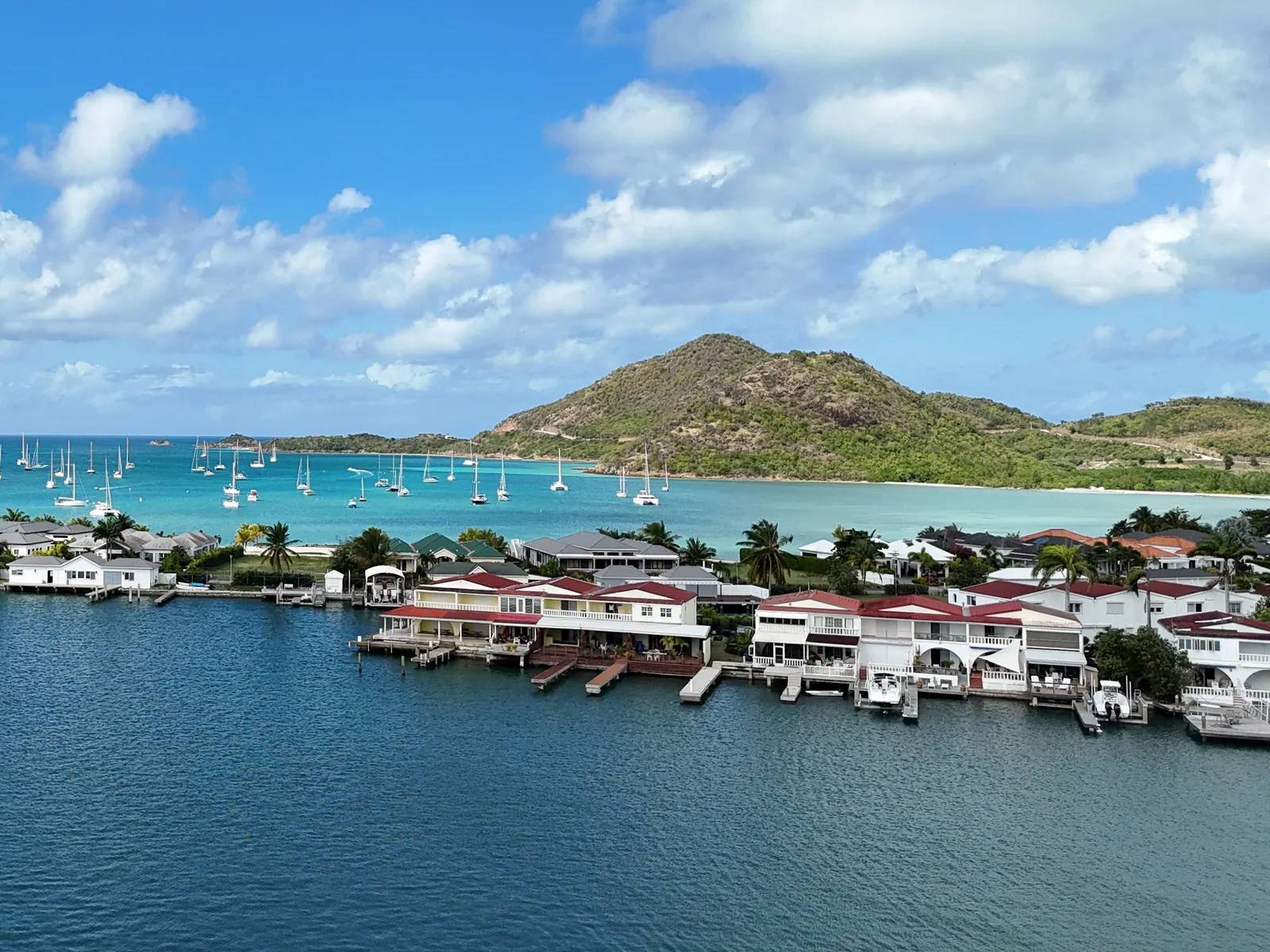 Waterfront homes with private docks at Jolly Harbour, Antigua, with yachts at anchor in the bay beyond